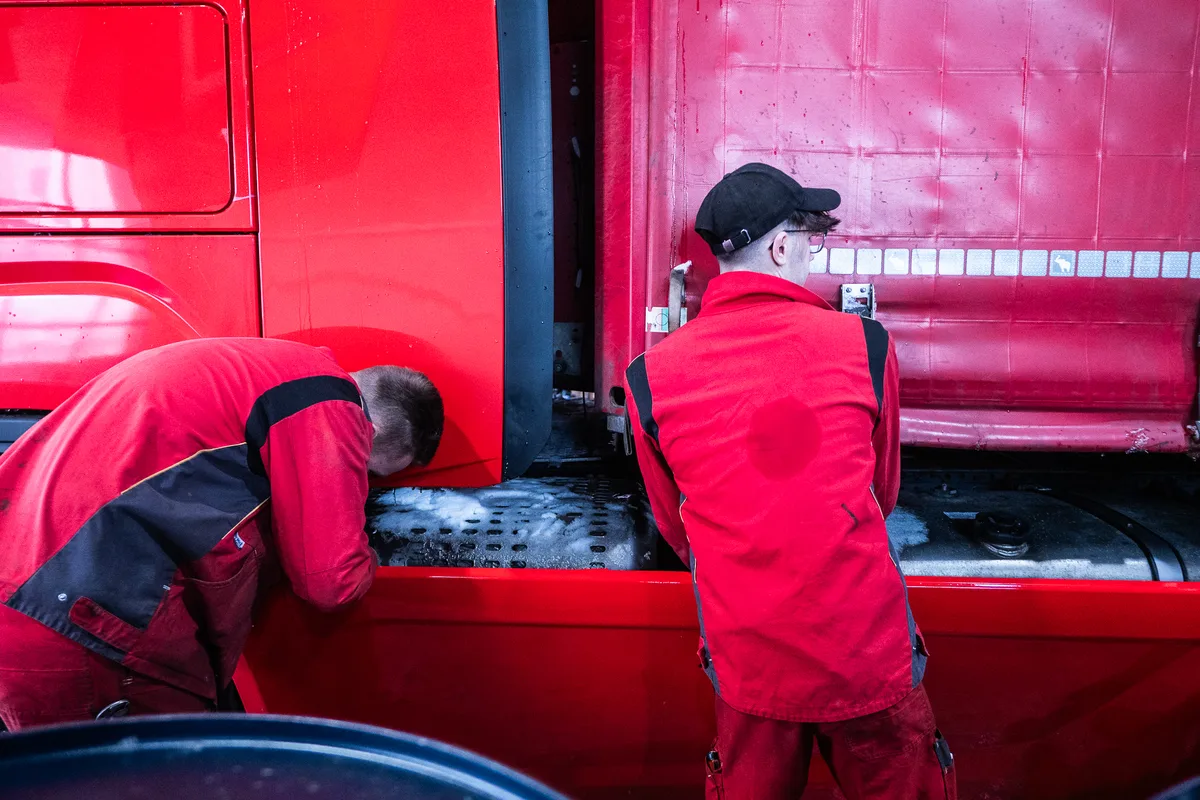 Zwei Mechaniker in roter Arbeitskleidung arbeiten an einem roten Sattelzug