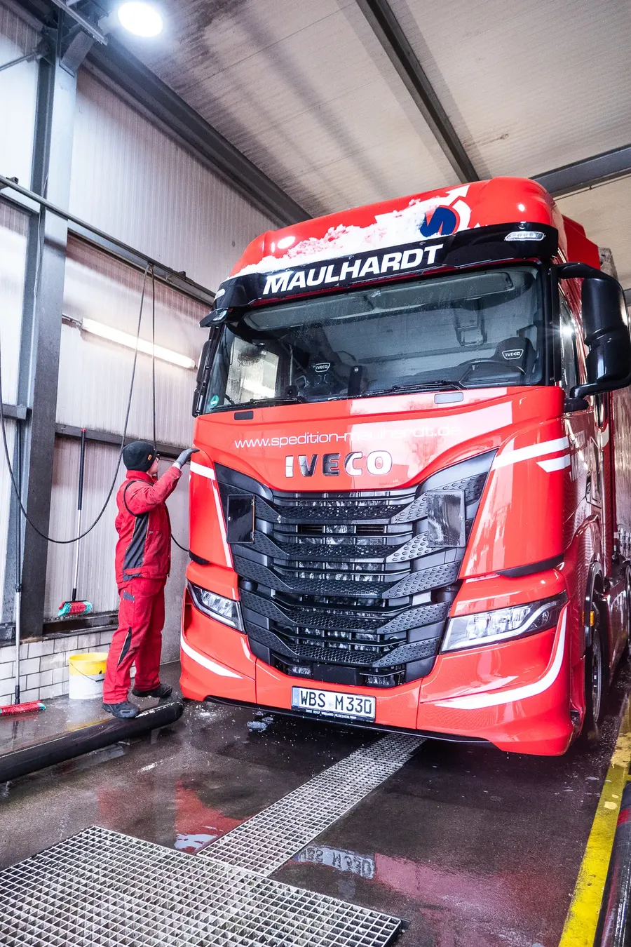 Mitarbeiter reinigt die Front eines IVECO-Sattelzugs in der Waschhalle von Hand