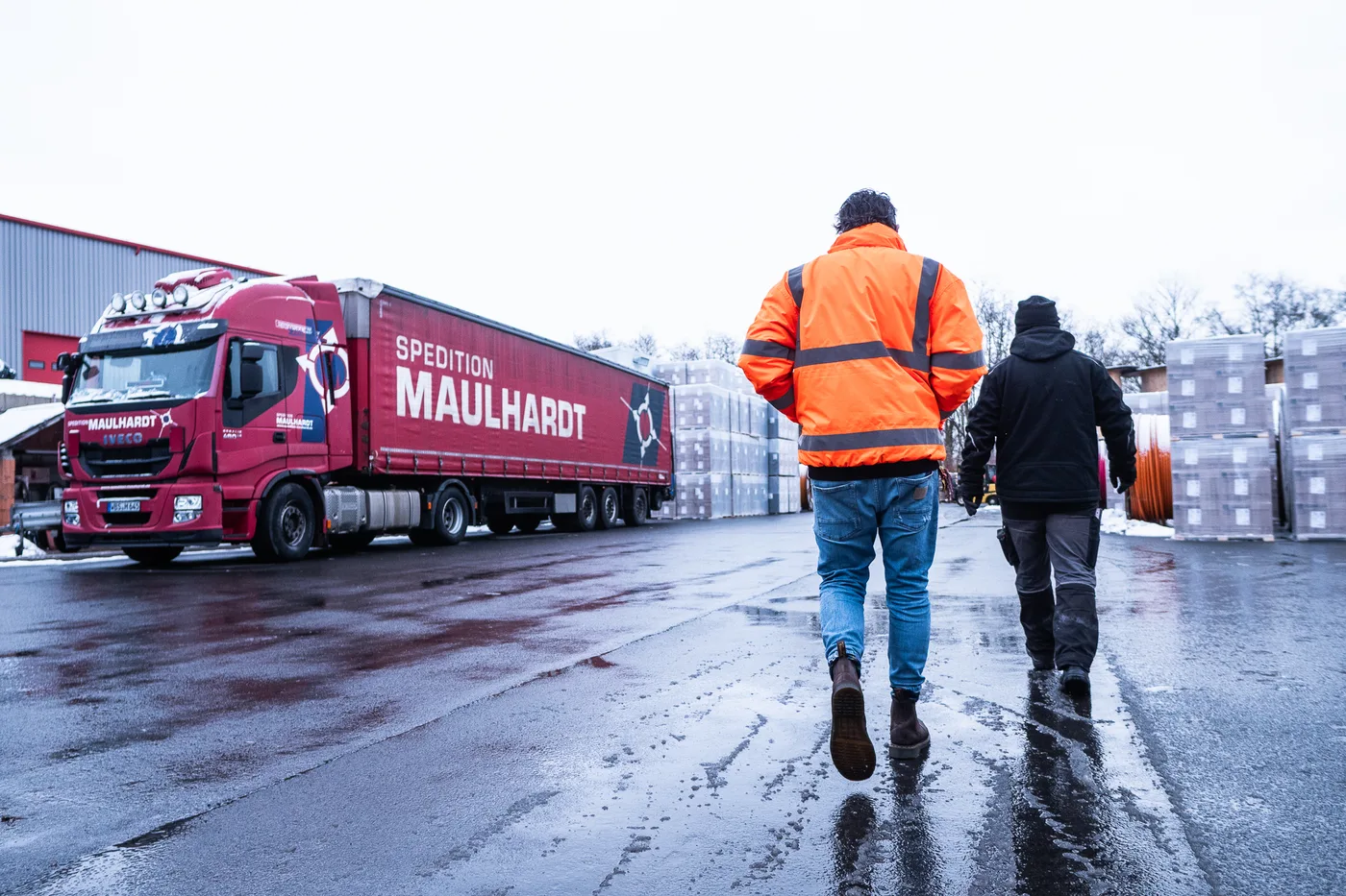 Zwei Mitarbeiter überqueren den Hof der Maulhardt Gruppe, links ein Sattelzug der Spedition