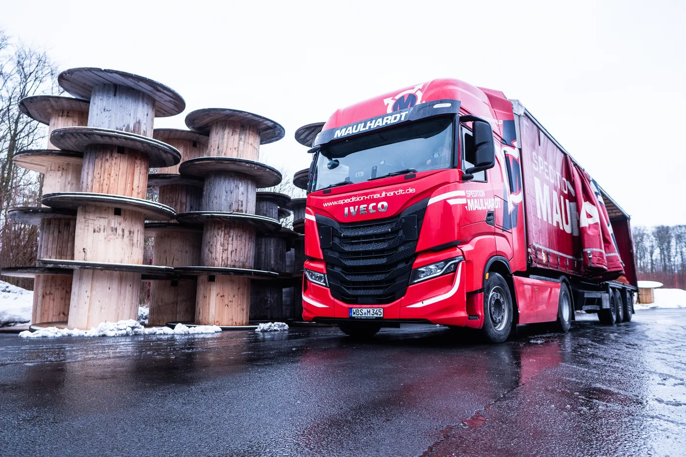 Roter Sattelzug der Spedition Maulhardt neben hoch gestapelten leeren Holztrommeln