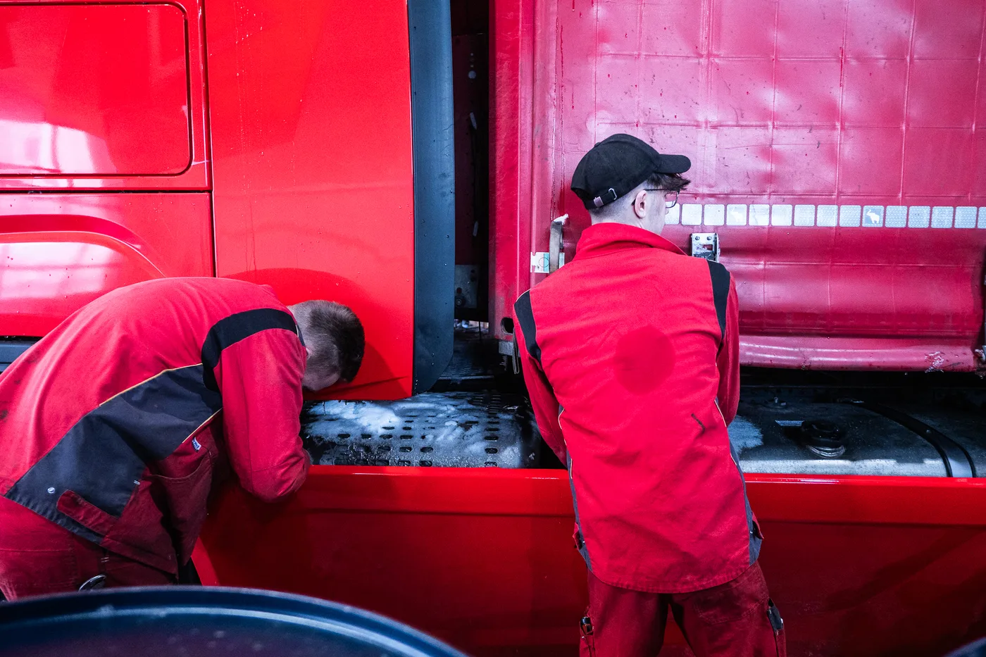 Zwei Mechaniker arbeiten zwischen Fahrerhaus und Auflieger eines roten Sattelzugs